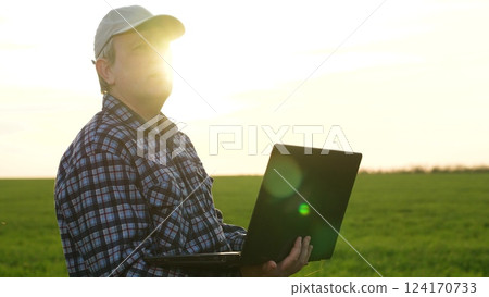 Modern man agronomist agricultural worker use laptop analyzing green wheat harvest outdoor at sunset closeup. Male farmer searching data examining cereal plant growth agriculture farmland cultivation 124170733