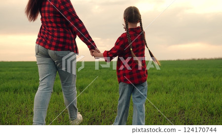 mother farmer leads child kid girl by hand through green field wheat sunset, family business, happy family sunset, parenting on farm, agricultural parenting moment, sunset farming life, happy farm 124170744