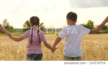 Happy boy and girl children walking with parents at sunny dry wheat field back view. Family kids brother and sister holding hands going at cereal agriculture harvest plantation enjoy freedom weekend Happy boy and girl children walking with parents at sunny dry wheat field back view. Family kids brother and sister holding hands going at cereal agriculture harvest plantation enjoy freedom weekend 124170758