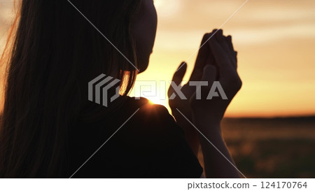 Woman praying with folded hands at sunset silhouette. Religious pious orthodox christian spiritual believing faithful girl at morning dawn sunrise reading prayer bible turning to god jesus christ. Woman praying with folded hands at sunset silhouette. Religious pious orthodox christian spiritual believing faithful girl at morning dawn sunrise reading prayer bible turning to god jesus christ. 124170764