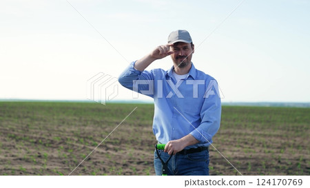 Male farmer smiling with shovel in field. Portrait man on background of field with green fresh corn crops, businessman worker holding shovel smiling broadly contentedly. Fun joyful working as farmer. 124170769