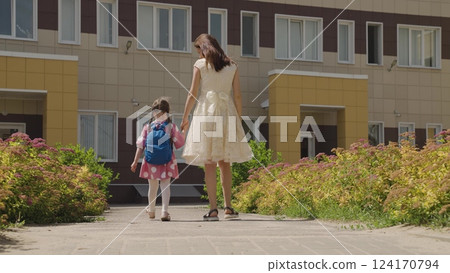 Mother leads little child kid daughter, holding hand, with backpack school, girl holding hand parent, mother, happy family, parent-child relationship, secure school walk, academic preparation, school 124170794