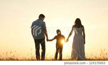 Family holding hands in field at sunset. Father dad kid boy child mother mom on golden rays sun go forward symbolizing hope bright future happy cheery memories time together. Strong family ties bonds 124170803