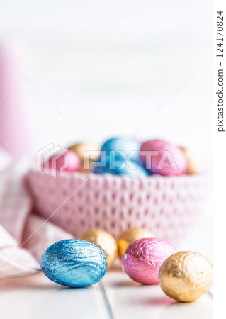 Chocolate easter eggs wrapped in multi colored foil on white table. 124170824