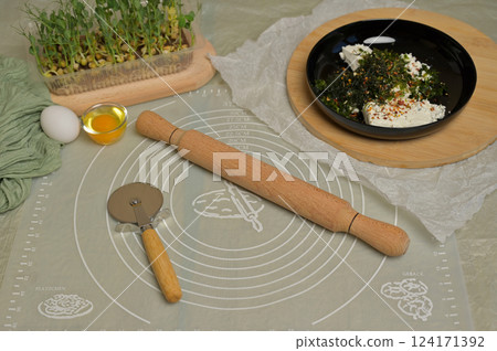 Rolling pin, cutter, eggs and microgreens sprouts on kitchen table. Parsley and dill greens with cottage cheese in a black bowl. Home cooking baking puffs Rolling pin, cutter, eggs and microgreens sprouts on kitchen table. Parsley and dill greens with cottage cheese in a black bowl. Home cooking baking puffs 124171392