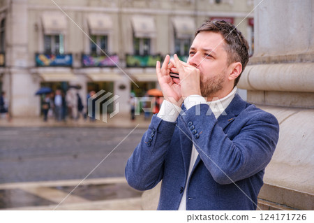 Man plays harmonica outdoors in city street 124171726