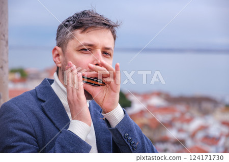 Man plays harmonica outdoors in city street 124171730