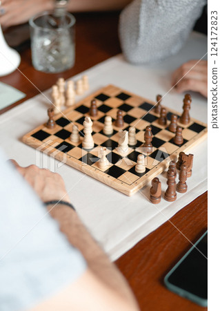 Engaging in an Intense Chess Game with Friends on a Classic Wooden Table in Leisurely Fun 124172823