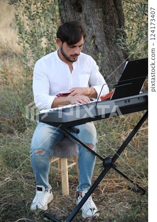 Boy Plays Music With Harmonica And Keyboard Among The Olive Trees Of Calabria 124173407