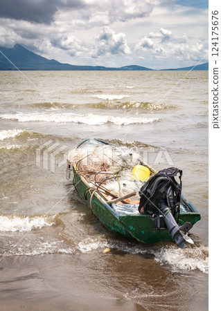 A fishing boat on the shore of a lake with volcanoes in the background. A fishing boat on a lake in Nicaragua. Concept of fishing boats parked at the seaside, Fishing boat on the shore of a lake 124175676