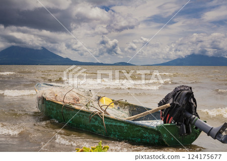 A fishing boat on a lake in Nicaragua. Concept of fishing boats parked at the seaside, Fishing boat on the shore of a lake, A fishing boat on the shore of a lake with volcanoes in the background 124175677