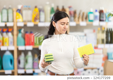 Woman in light clothes choosing sponges to wash dishes in supermarket 124177209