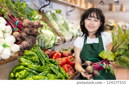 Smiling young saleswoman holding beetroots in grocery store Smiling young saleswoman holding beetroots in grocery store 124177335