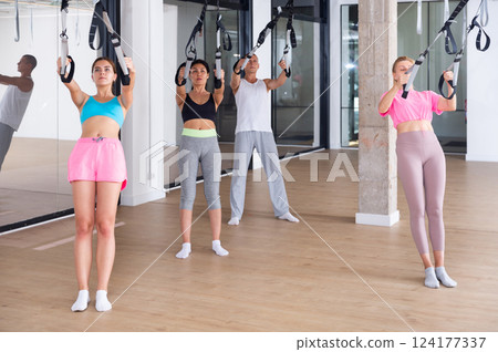 Sports people perform an exercise for stretching muscles using a special suspended structure Sports people perform an exercise for stretching muscles using a special suspended structure 124177337