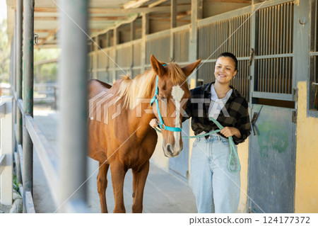 Young woman leads horse out of stable 124177372