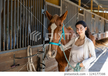 Young woman leads horse out of stable 124177386