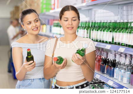 Young women discussing choice of alcoholic drinks in supermarket Young women discussing choice of alcoholic drinks in supermarket 124177514