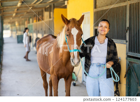 Young woman leading horse out of stable Young woman leading horse out of stable 124177603