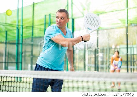 Concentrated man padel player hitting ball with racket Concentrated man padel player hitting ball with racket 124177840