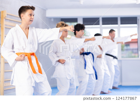 Teenager in kimono practicing punches during group martial arts workout 124177867