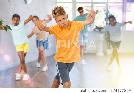Positive juvenile boy engaged in Breakdancing in training room with children's group Positive juvenile boy engaged in Breakdancing in training room with children's group 124177899