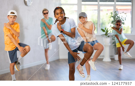 Positive juvenile boy engaged in Breakdancing in training room with children's group 124177937