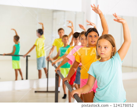 Focused tween girl practicing ballet positions near bar during group class Focused tween girl practicing ballet positions near bar during group class 124178052
