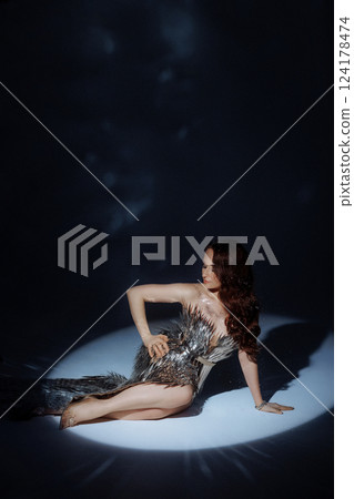 A woman in a metallic gown poses under a focused light. 124178474