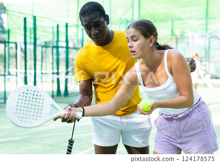 Girl learning to play padel tennis with male trainer 124178575