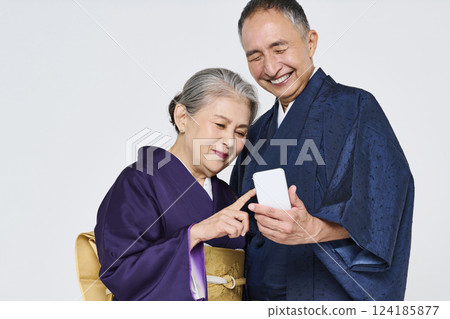 Senior couple wearing kimonos using smartphones together 124185877