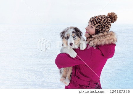 Woman holds a little cute Australian Shepherd puppy in blue marble color and different eye color. Copy space photo back view, snow landscape Woman holds a little cute Australian Shepherd puppy in blue marble color and different eye color. Copy space photo back view, snow landscape 124187256