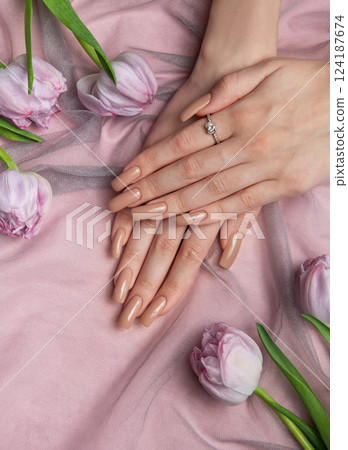 Woman showing nude manicure and diamond ring near tulips on pink cloth Woman showing nude manicure and diamond ring near tulips on pink cloth 124187674