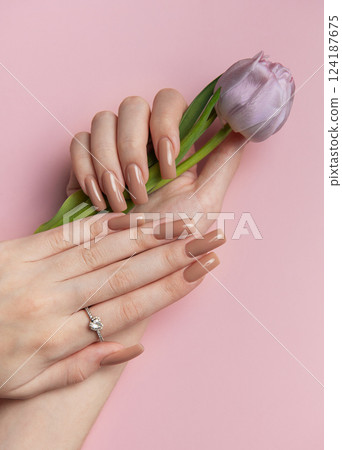 Woman showing manicure and holding a purple tulip on pink background Woman showing manicure and holding a purple tulip on pink background 124187675