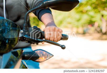 Close up of the hands on the handlebars of a motorcycle. Hands of a person on the motorcycle handlebars. Motorbike speeding concept, Hands of a motorcyclist on the handlebars 124189297