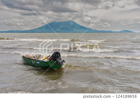 A wooden fishing boat on the shore of a lake, Nicaragua. Fishing boat on the shore of a lake, A fishing boat on the shore of a lake with volcanoes in the background 124189658
