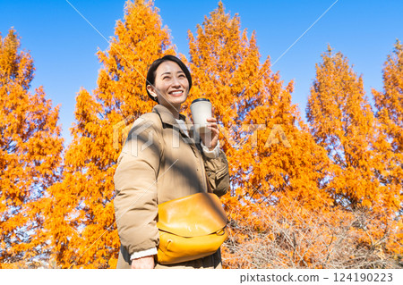 Woman drinking a hot drink while enjoying the autumn leaves Lifestyle image 124190223