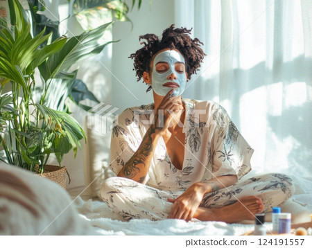 Non-binary individual applying a face mask in a serene home setting, surrounded by natural light and sustainable skincare products 124191557