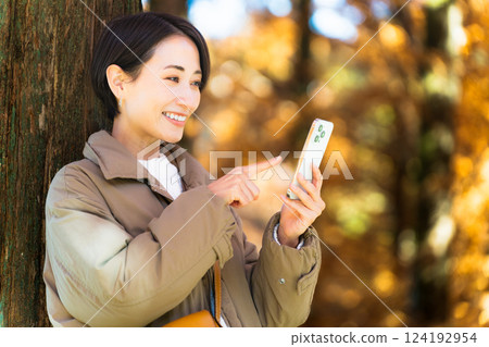 一位女士一邊使用智慧型手機一邊欣賞秋葉 生活風格圖片 一位女士一邊使用智慧型手機一邊欣賞秋葉 生活風格圖片 124192954