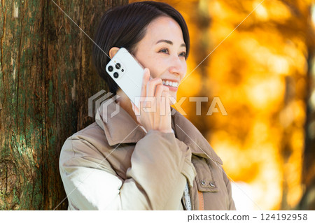 一位女士一邊打電話一邊欣賞秋葉 生活方式圖像 一位女士一邊打電話一邊欣賞秋葉 生活方式圖像 124192958