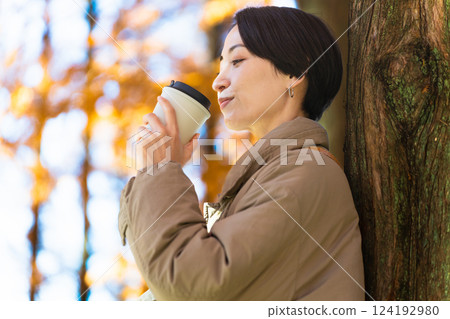 Woman drinking a hot drink while enjoying the autumn leaves Lifestyle image 124192980