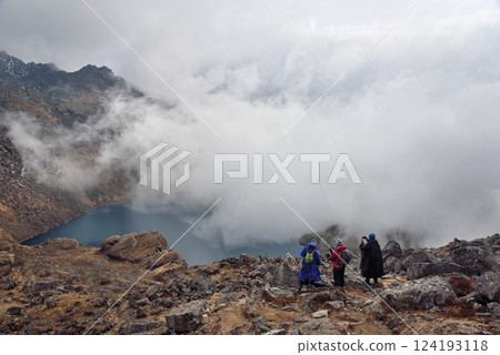 Three people on a mountain top over a Gosaikunda lake 124193118