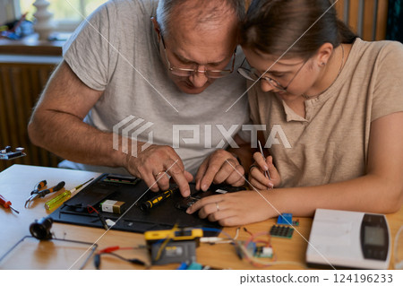 Grandfather and granddaughter work together on an electronics project 124196233
