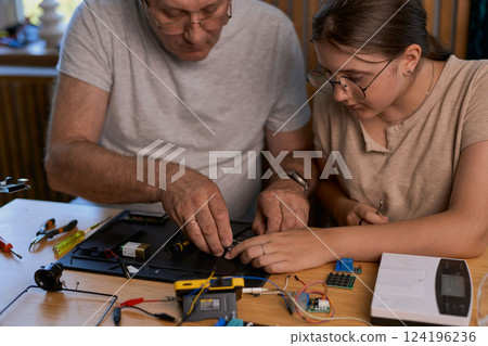 Grandfather and granddaughter work together on an electronics project Grandfather and granddaughter work together on an electronics project 124196236