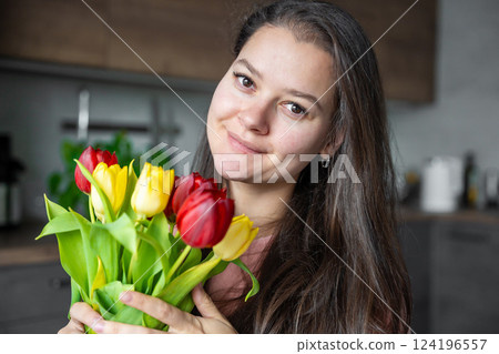 Portrait of young woman with a bouquet of red and yellow tulips at home. Congratulations and a gift on International Women's Day or Mother's Day Portrait of young woman with a bouquet of red and yellow tulips at home. Congratulations and a gift on International Women's Day or Mother's Day 124196557