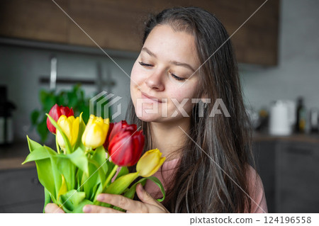 Young woman with a bouquet of red and yellow tulips at home. Congratulations and a gift on International Women's Day or Mother's Day Young woman with a bouquet of red and yellow tulips at home. Congratulations and a gift on International Women's Day or Mother's Day 124196558