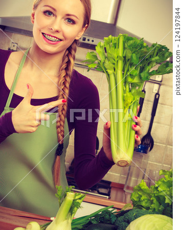 Woman in kitchen holds green celery Woman in kitchen holds green celery 124197844