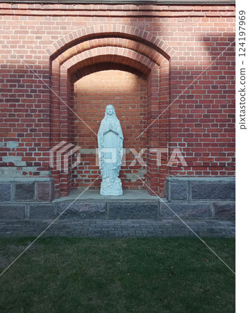 A white statue of the Virgin Mary placed within an arched alcove of a historic red brick church wall in Belarus. A white statue of the Virgin Mary placed within an arched alcove of a historic red brick church wall in Belarus. 124197969