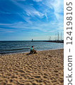 Woman relaxing in a deckchair on the beach overlooking the lighthouse and marina on a sunny day on Lake Vattern, Sweden 124198105
