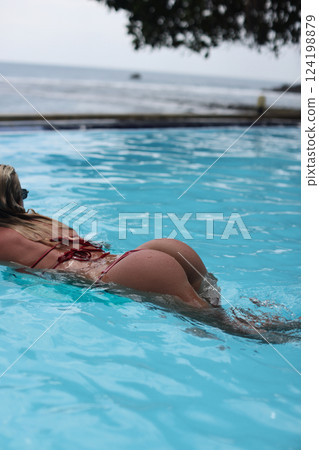 A woman enjoying swimming in a beautifully clear pool located by the vast ocean shores 124198879