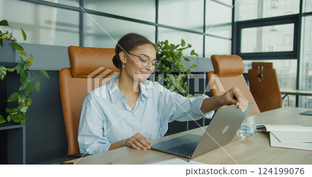 smiling young woman in glasses sitting at a modern office desk, closing her laptop while enjoying a productive day in a clean, professional, and stylish workspace smiling young woman in glasses sitting at a modern office desk, closing her laptop while enjoying a productive day in a clean, professional, and stylish workspace 124199076
